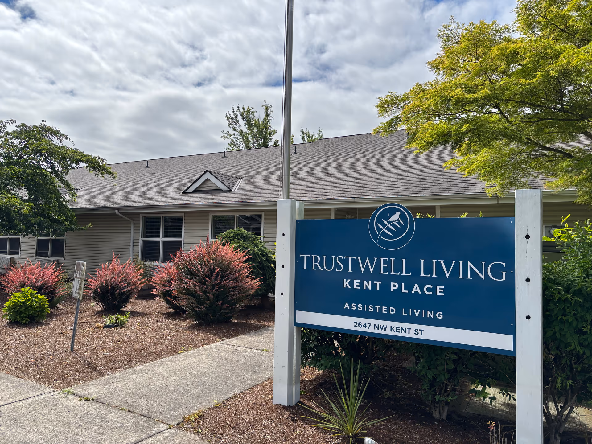 Exterior view of Trustwell Living at Kent Place with a blue sign and landscaped front yard.