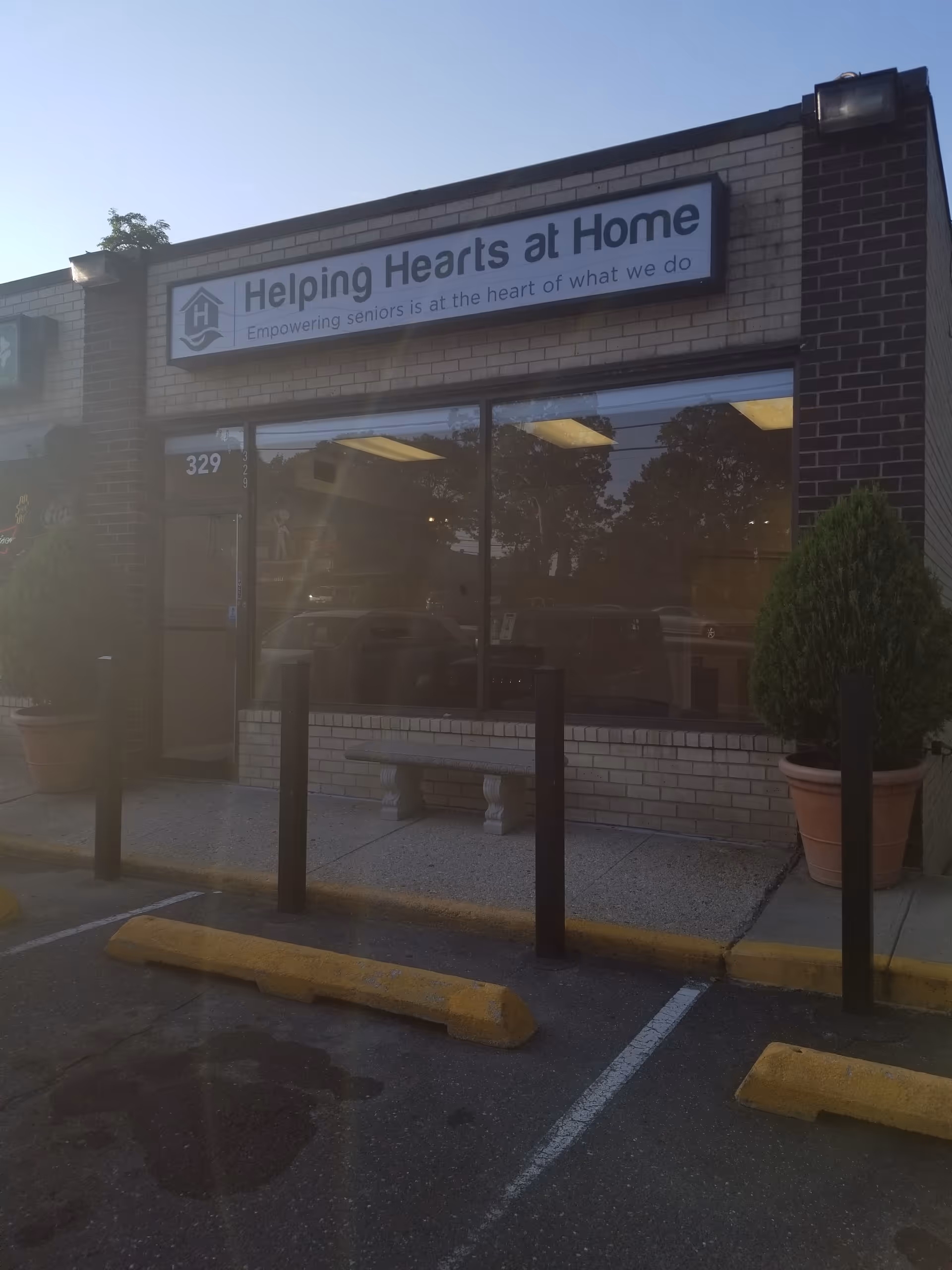 Exterior storefront of Helping Hearts at Home with sign, windows, bench, and planters.