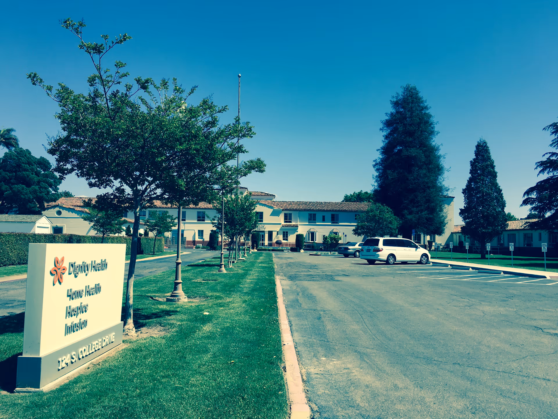 Front exterior of a Dignity Health facility with sign, trees, and a parking lot.
