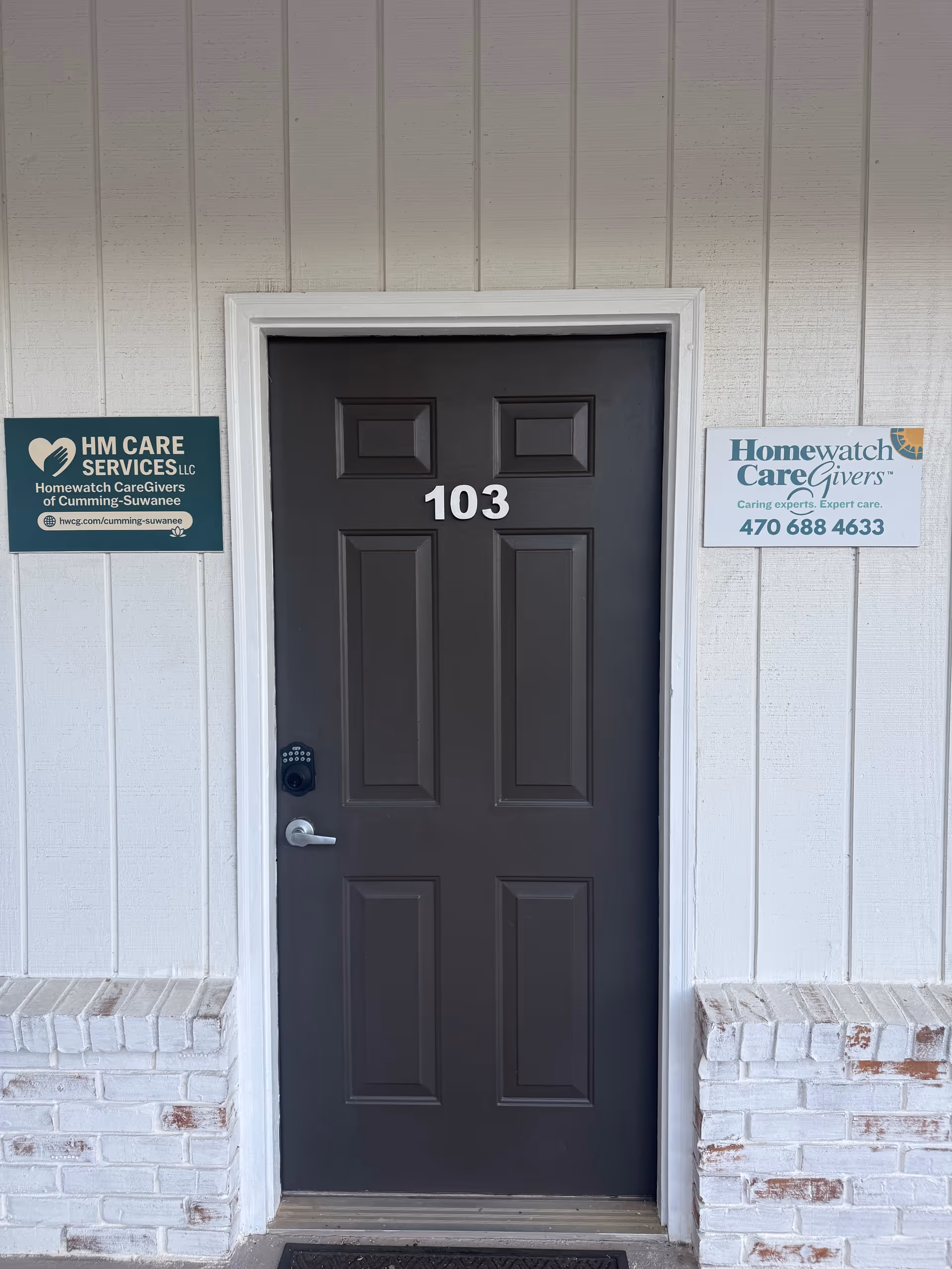 Dark gray front door numbered 103 with exterior siding and two care signs beside it.