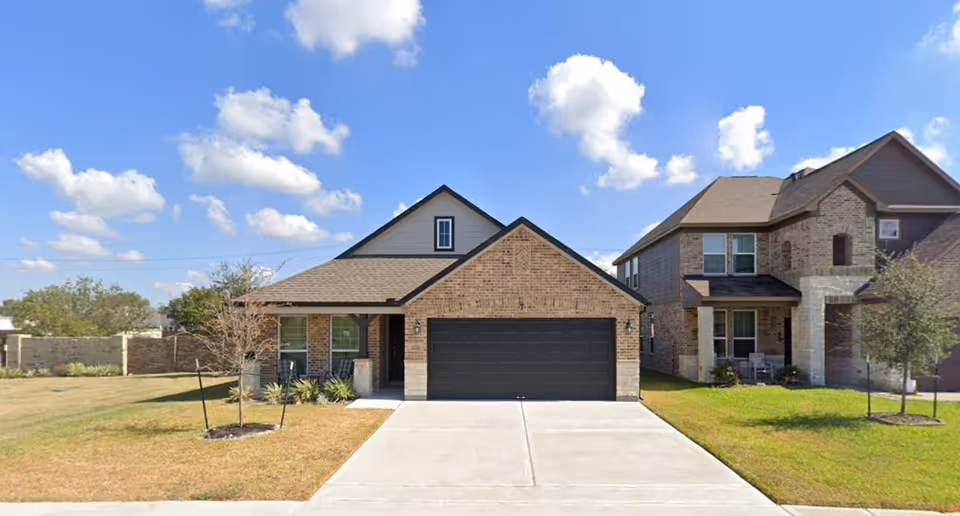 Front exterior of a brick house with a two-car garage and manicured lawn.