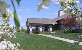 Front view of Clement Manor Retirement Community building with green lawn and blooming trees.