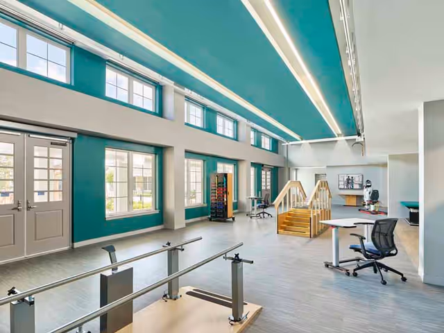 Interior view of a senior living facility with teal walls, windows, and exercise equipment.
