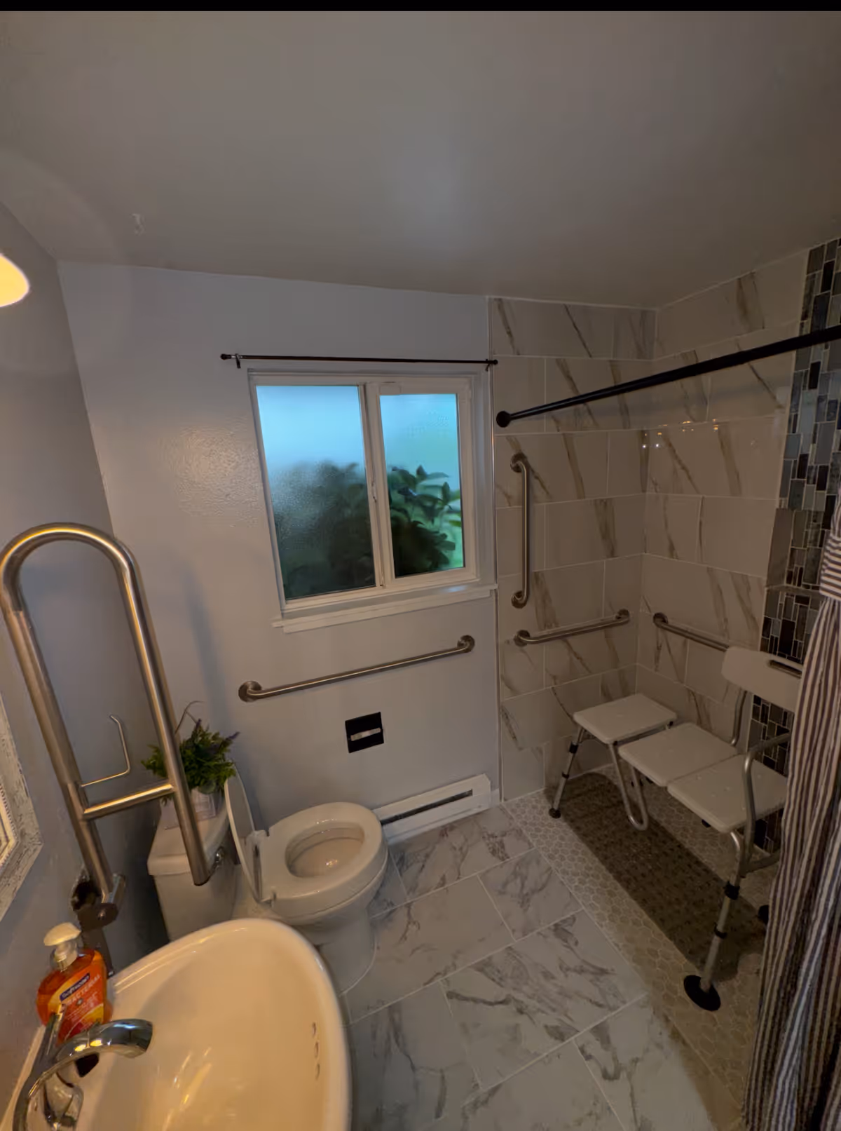 Accessible bathroom with grab bars, a tiled shower stall with chairs, sink, and toilet.