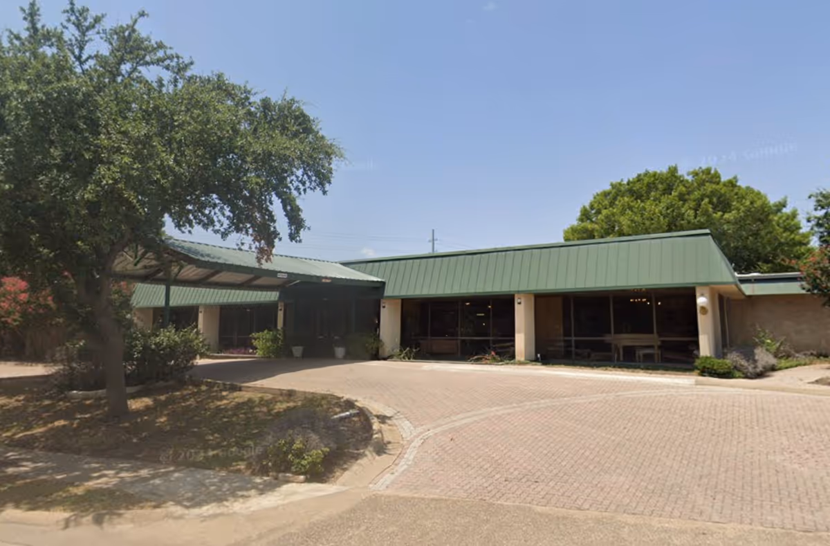 Exterior view of a single-story building with a green roof and brick-paved driveway.