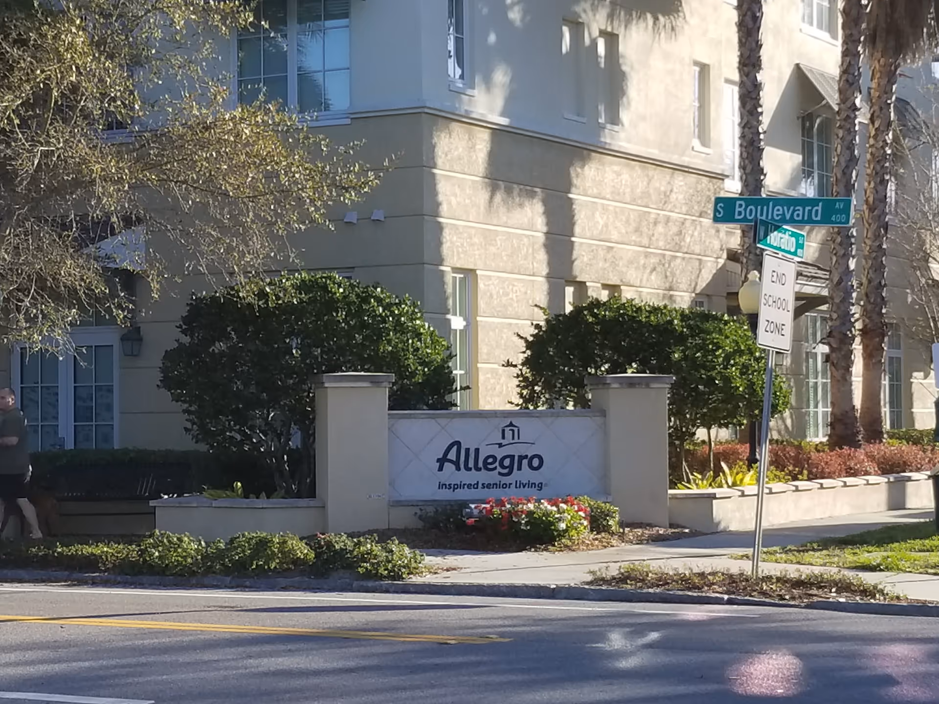 Exterior view of Allegro Senior Living building with sign, landscaping, and street corner.