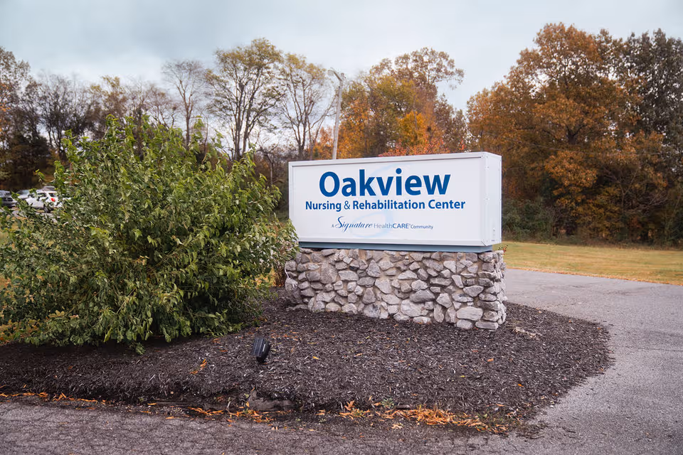 Oakview Nursing & Rehabilitation Center sign atop a stone pedestal outdoors among trees.