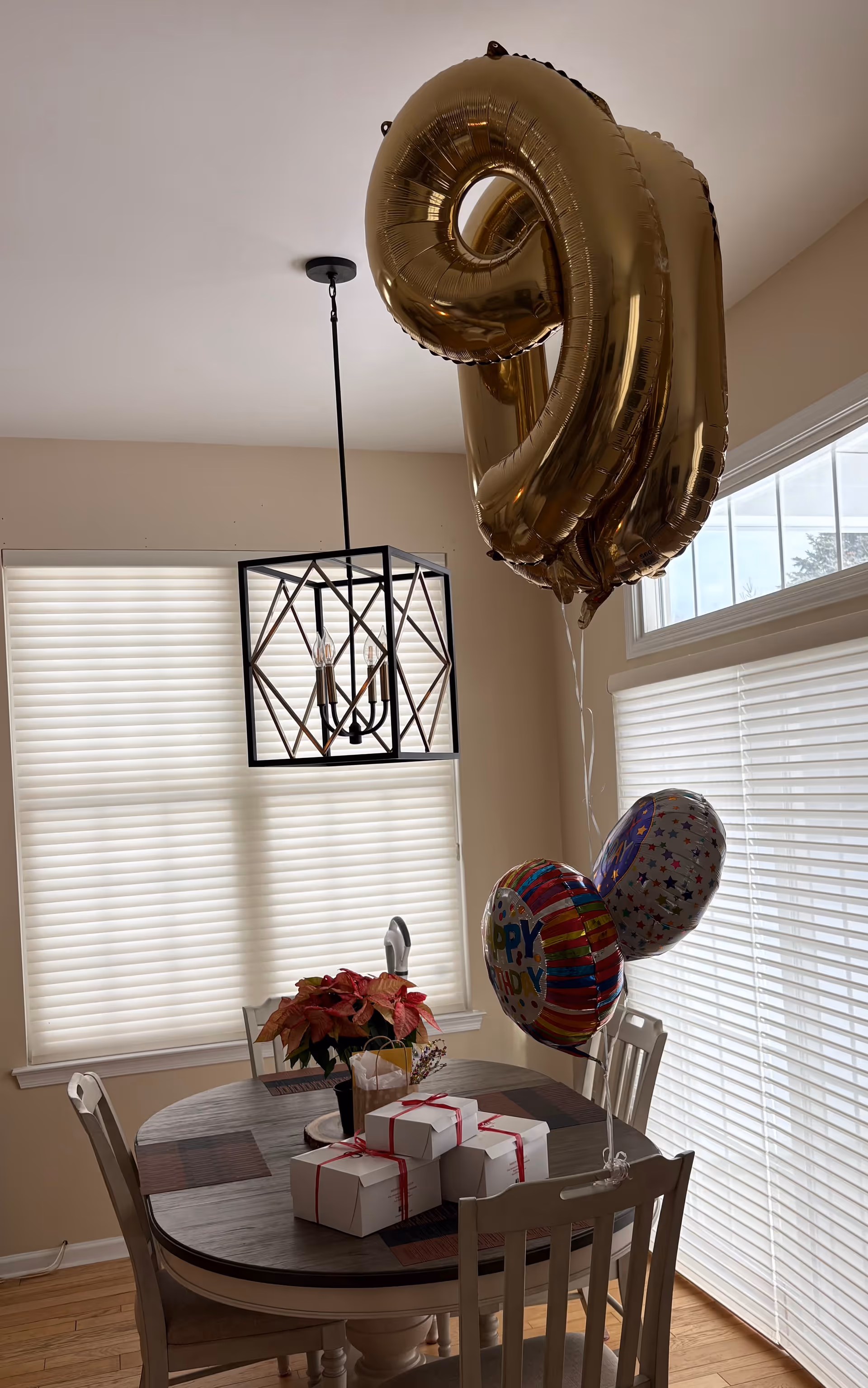 A round dining table with balloons, gifts, and a poinsettia in a bright dining room.