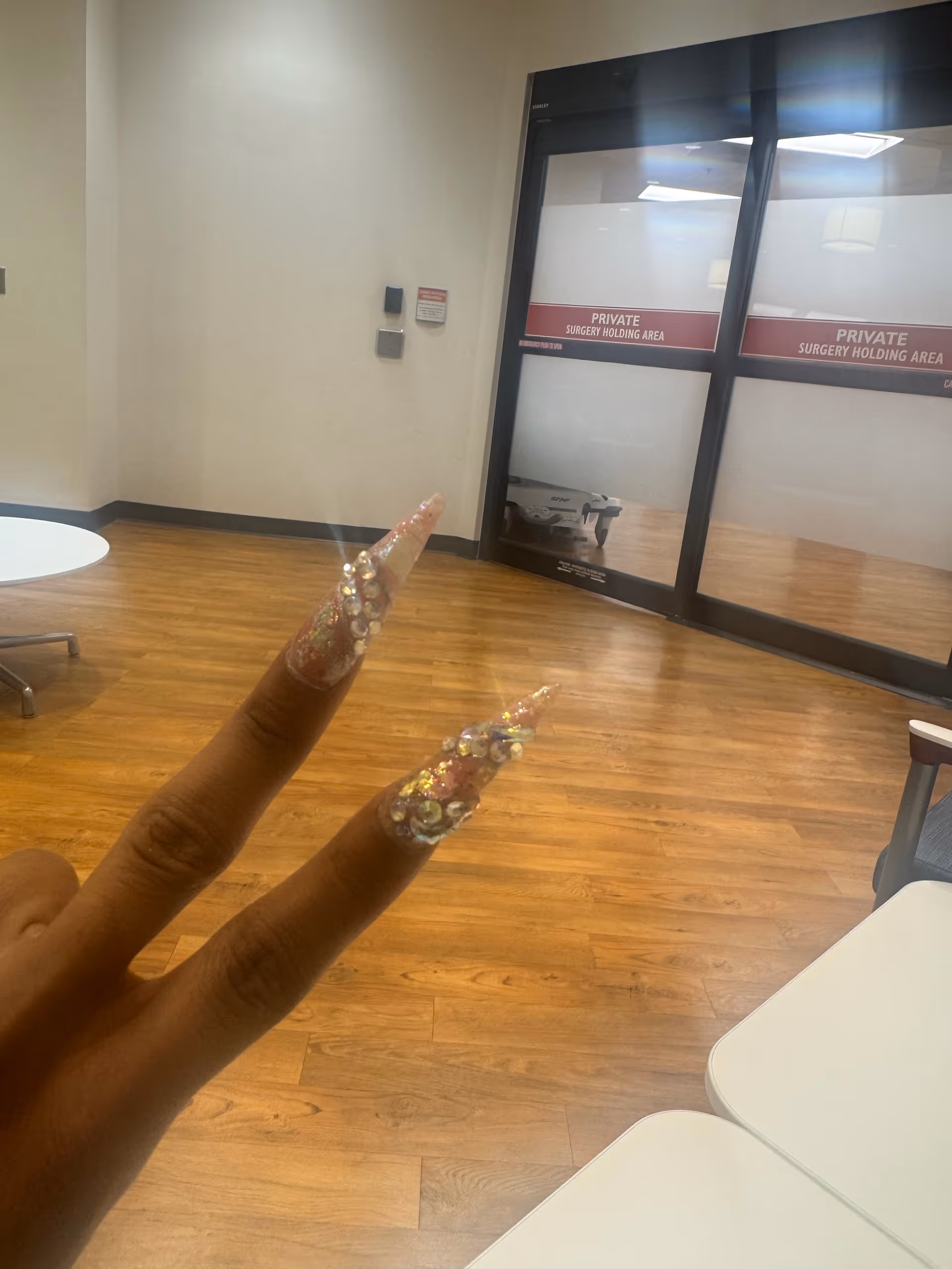 Hand with long glittery nails in a facility hallway near glass doors labeled private surgery area.