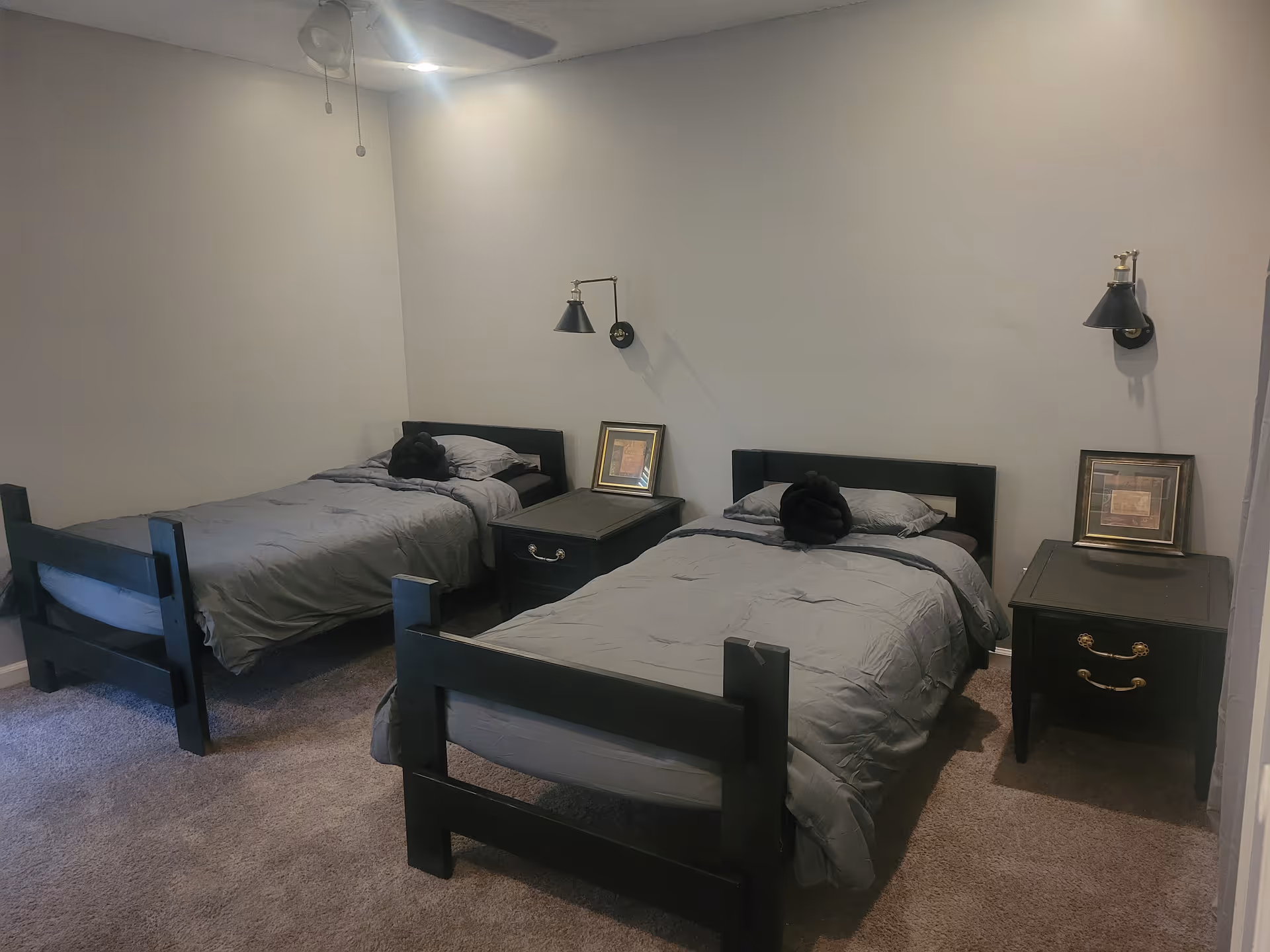 Two twin beds with gray comforters and nightstands in a small, carpeted bedroom.