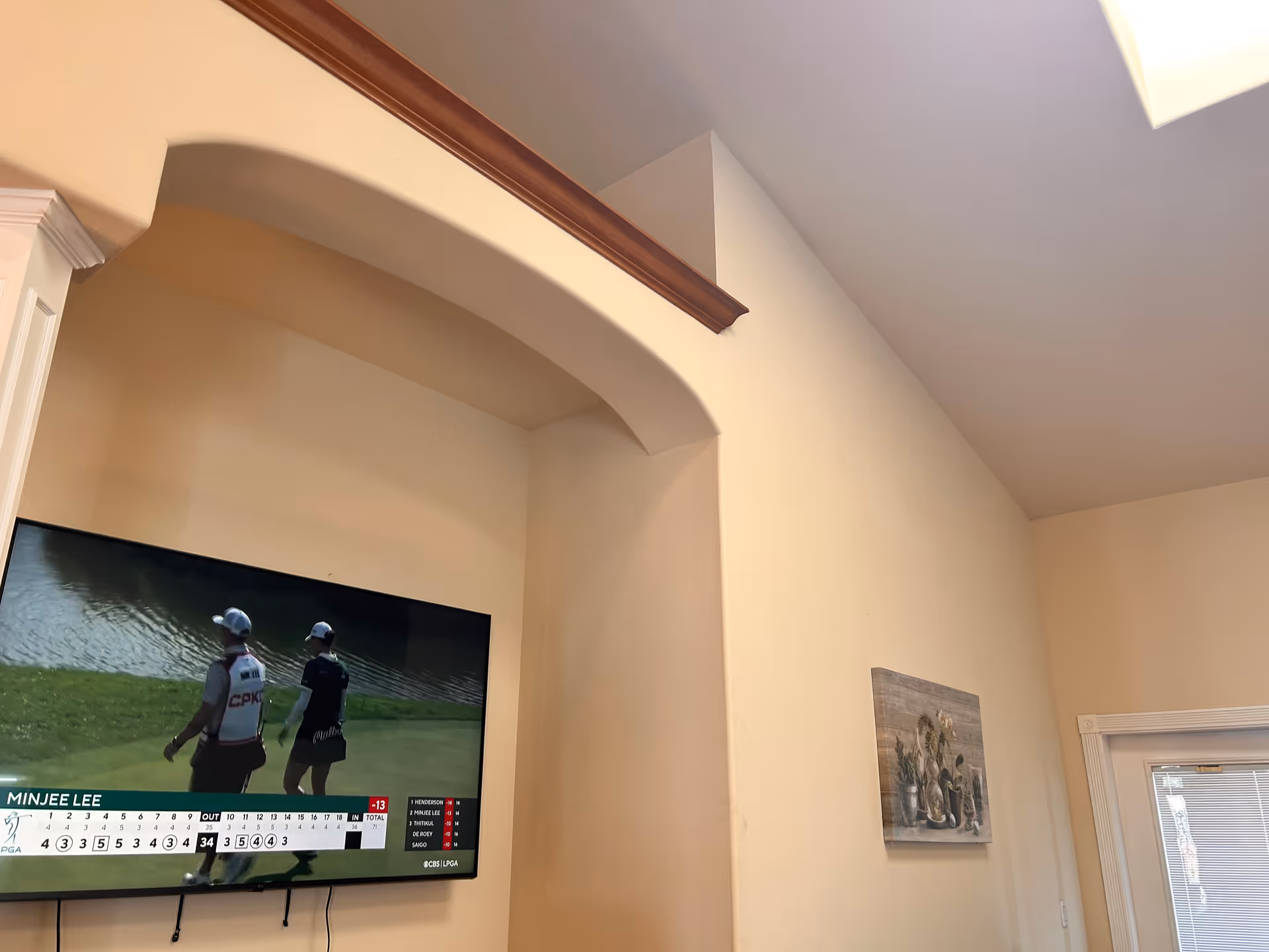 Living room with a wall-mounted TV showing golf, arched entry, and beige walls.