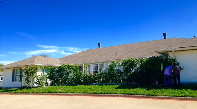 Exterior view of a single-story Hamilton Parc facility with vines and two people by entrance