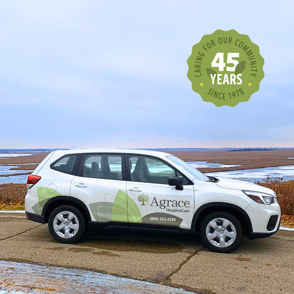 White Agrace HospiceCare SUV parked outdoors by a river under a blue sky