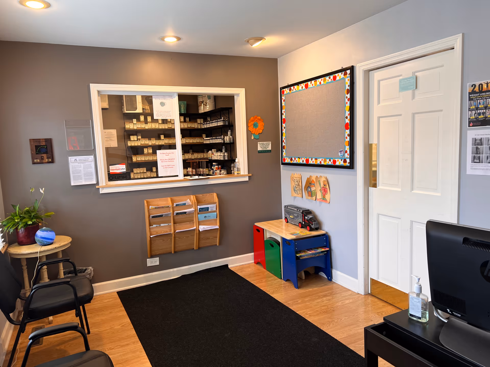 Interior reception area with a medication counter, bulletin board, children's play corner, and desk.