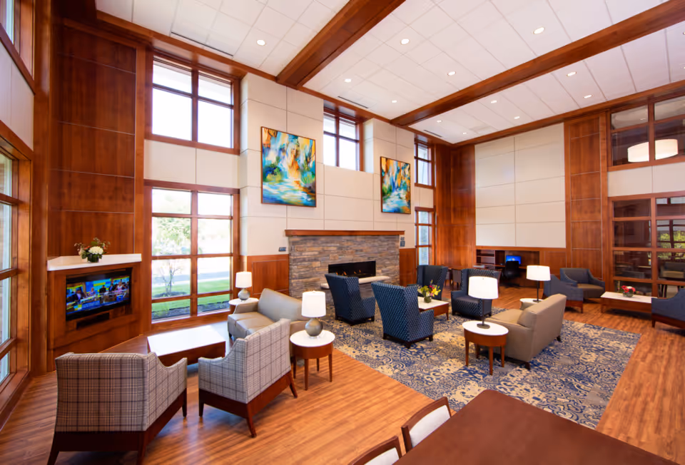 Spacious indoor senior living lounge with wood paneling, fireplace, and assorted seating.
