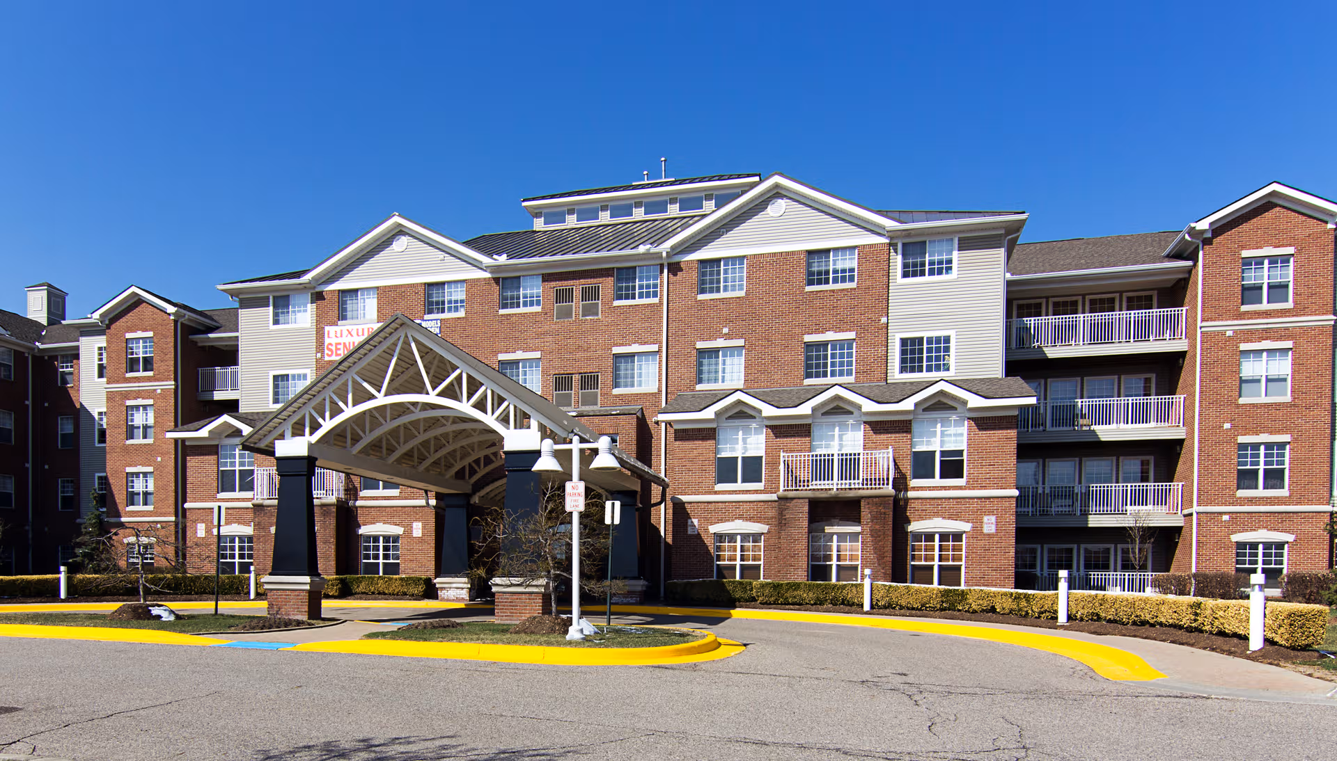 Brick senior living building with a large decorative entrance canopy and balconies.