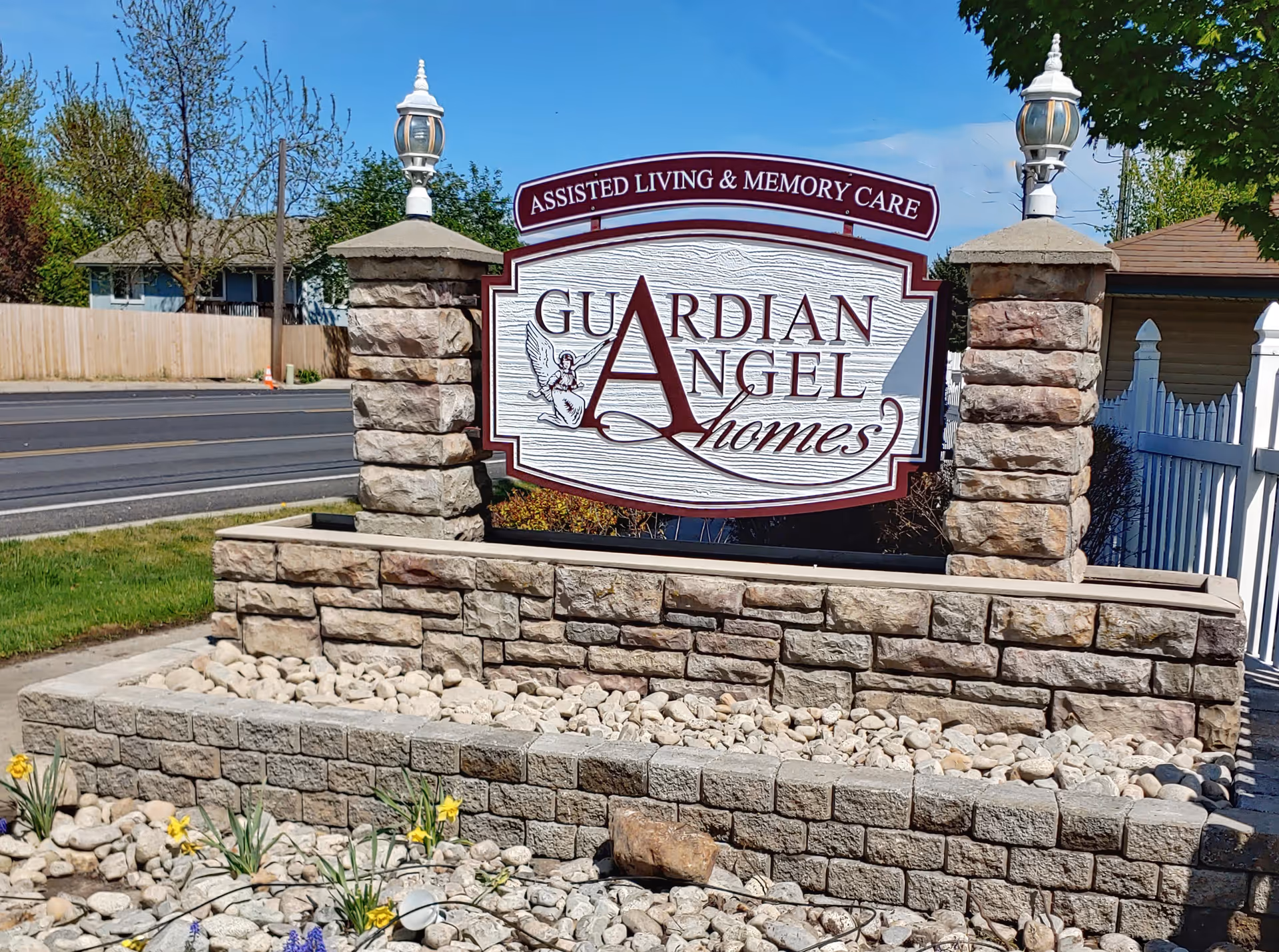 Stone front sign reading Guardian Angel Homes with surrounding landscaping and lamps.