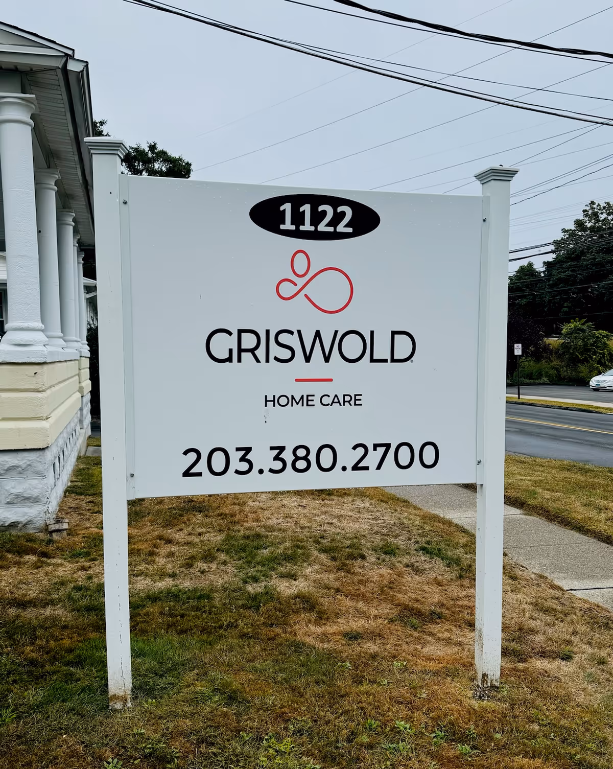 White Griswold Home Care sign on a lawn with 1122 and phone number.