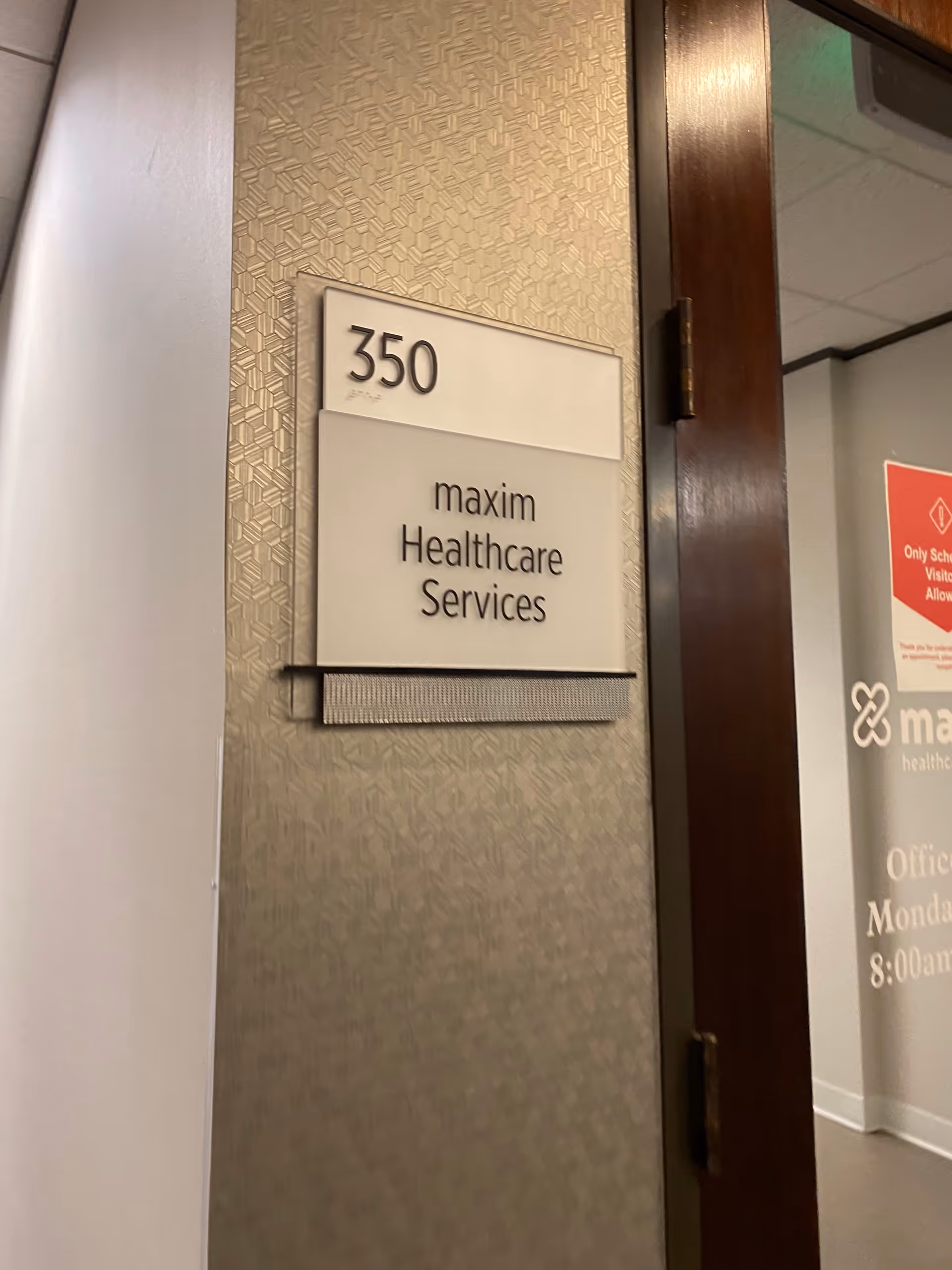 Interior hallway with wall sign reading 350 Maxim Healthcare Services beside a doorway.