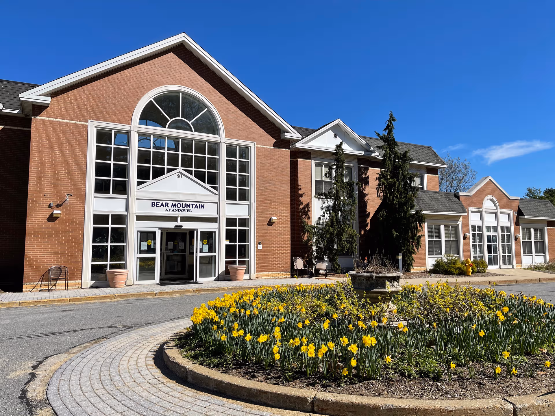 Exterior view of Bear Mountain at Andover entrance with a flower bed and bright blue sky.