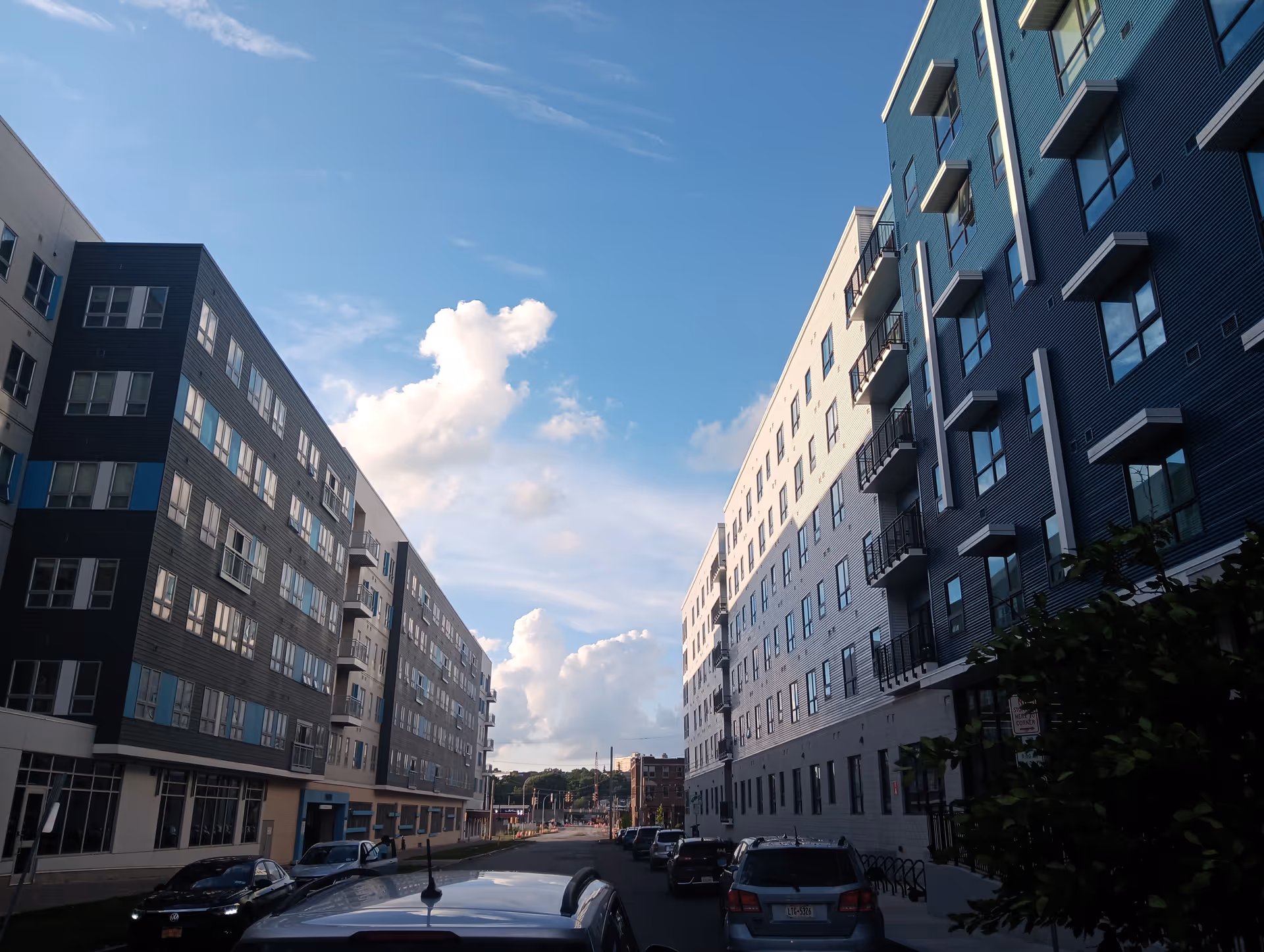 Exterior view of South Crouse Commons: tall modern buildings lining a street with parked cars.