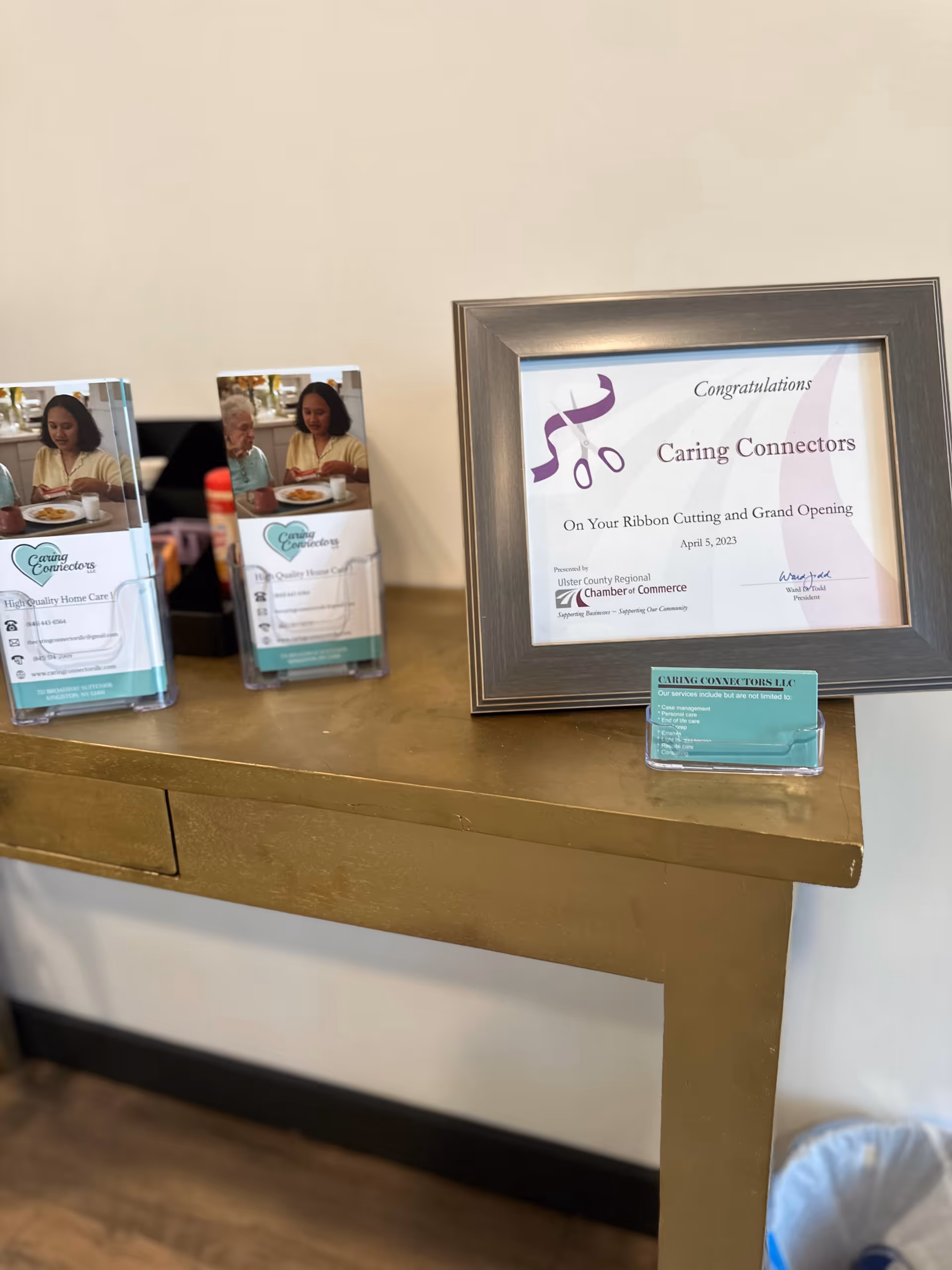 Framed Caring Connectors certificate beside brochures on a wooden console table.