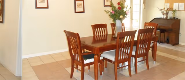 Wood dining table with six chairs in a well-lit senior living dining room.