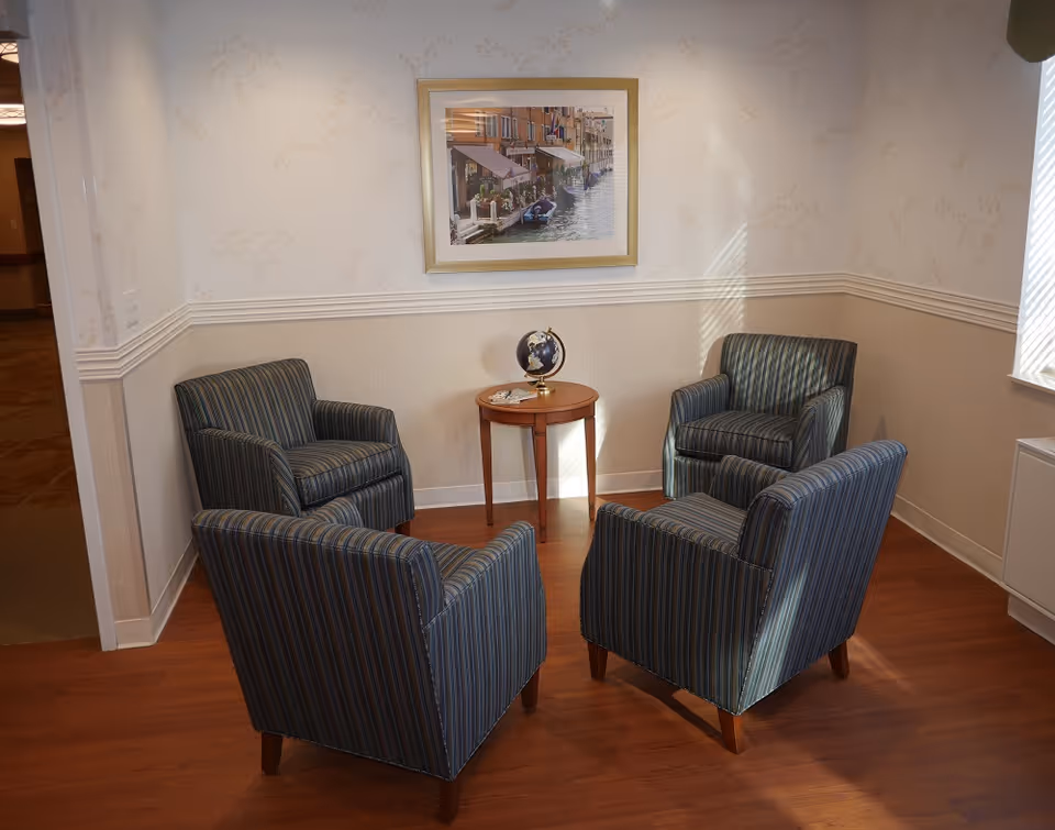 Four blue striped armchairs surround a round wooden table in a small lounge.