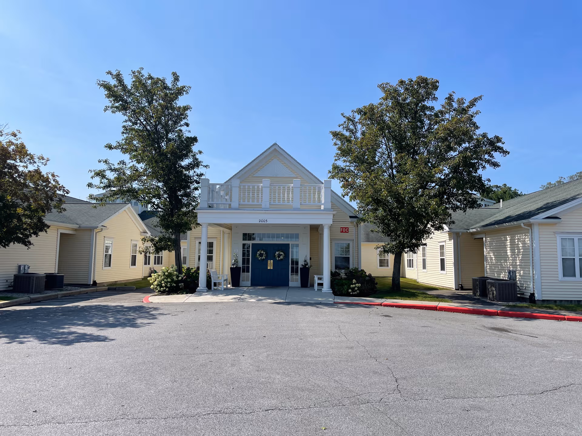 Front view of The Atrium at Faxon Woods entrance with beige buildings and trees.