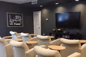 Cozy lounge with beige chairs around small tables and a wall-mounted TV.