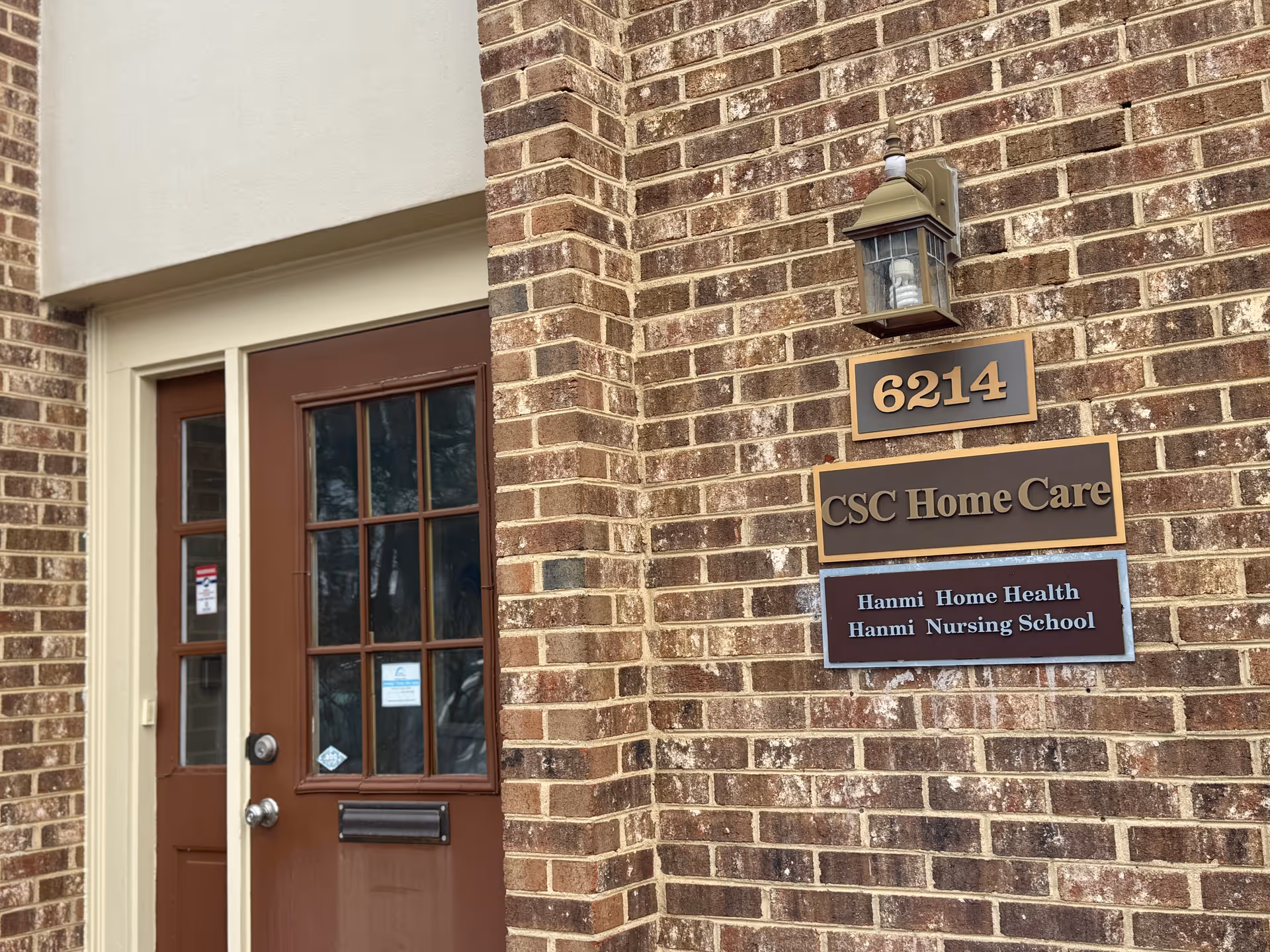 Brick building entrance with brown door and signs for Hanmi Home Health and CSC Home Care