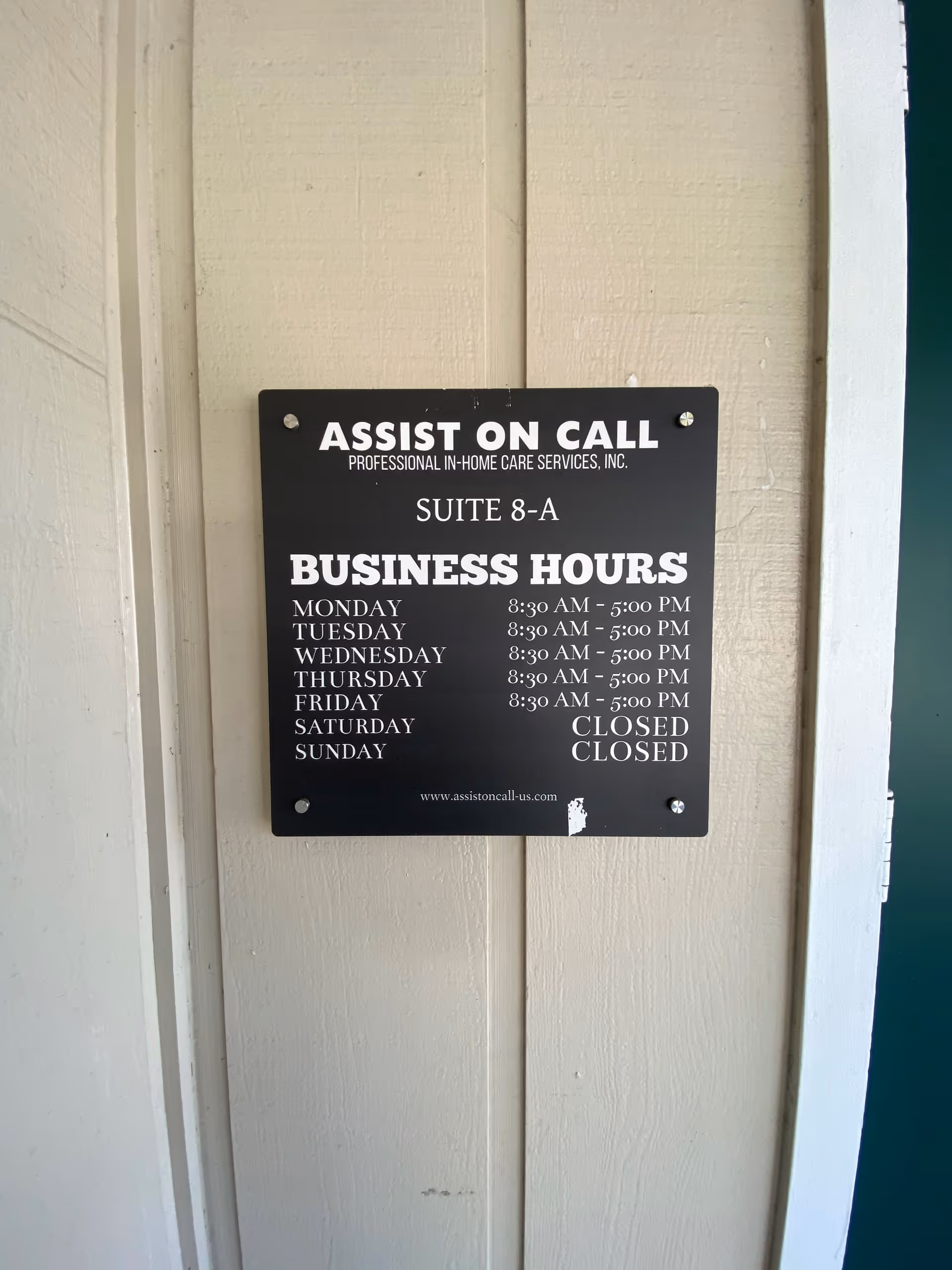 Black business hours sign mounted on beige exterior wall near a doorway