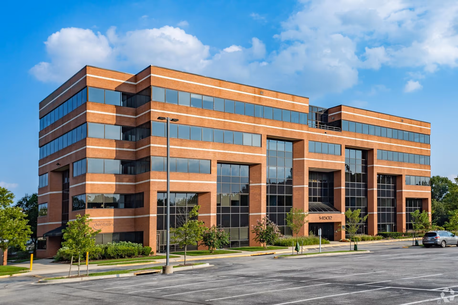 A modern brick office building with large glass windows and a parking lot.