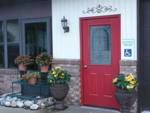Entrance of a senior living facility with a red door and potted flowers.