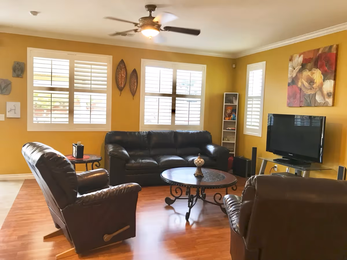 Sunlit living room with leather sofa and armchairs around a round coffee table, a flat-screen TV, and yellow walls.