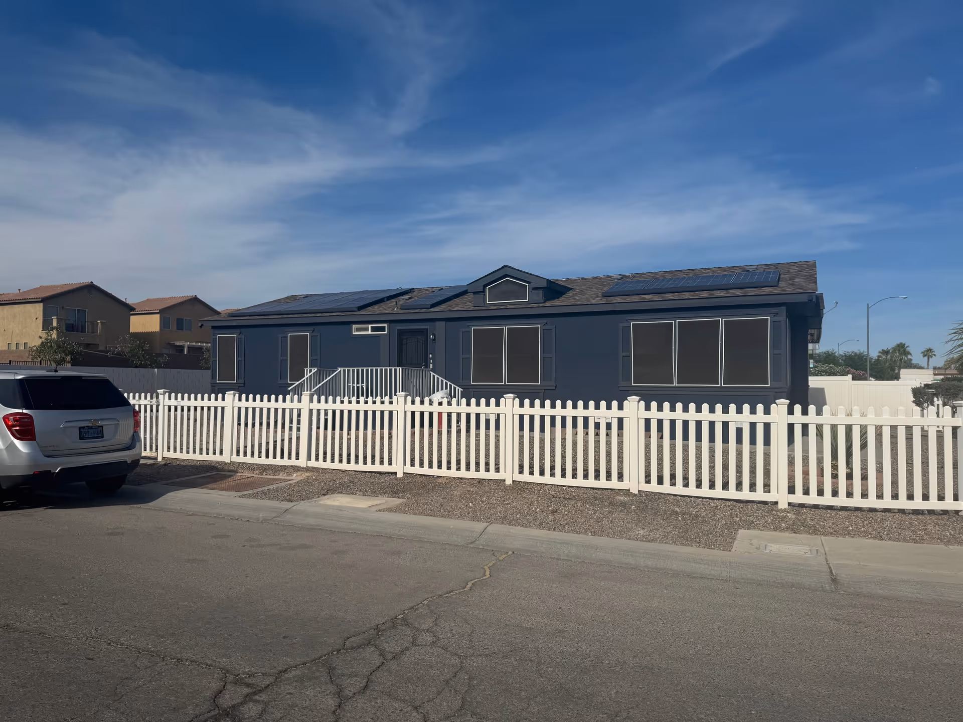 Dark blue single-story building behind a white picket fence with a parked car.