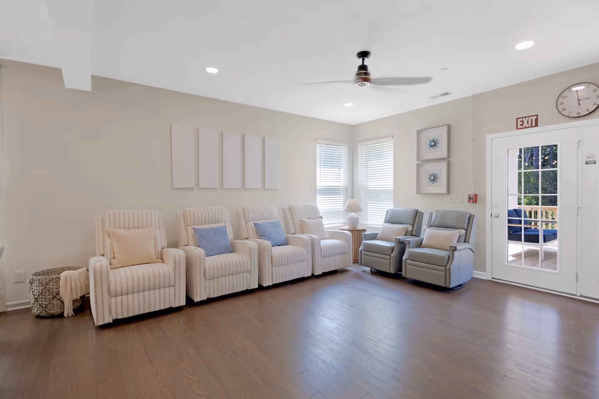Bright senior living lounge with striped armchairs, recliners, and an exit door.