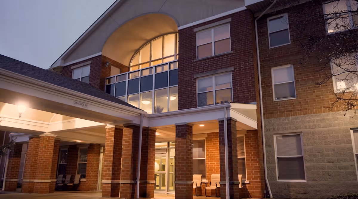 Brick senior living facility exterior with glass lobby, entry canopy, and seating.