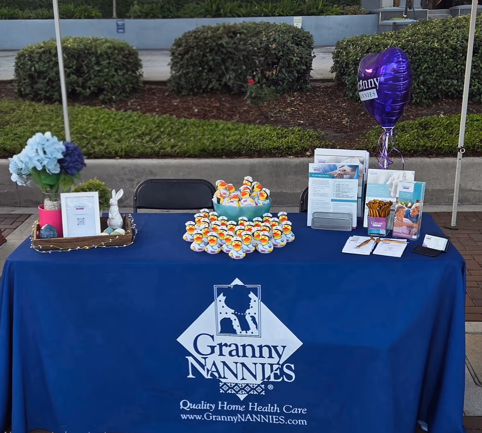 Outdoor table with Granny Nannies promotional materials, balloon, and duck-shaped treats.