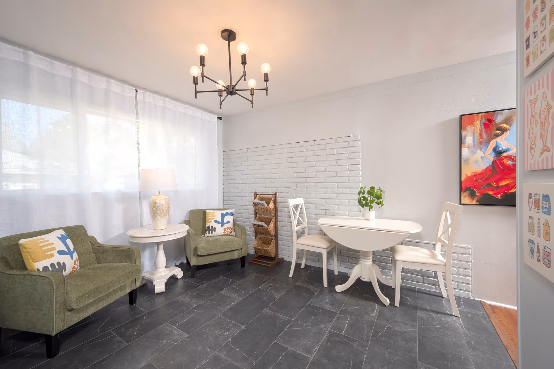 Bright senior living lounge with two green chairs, a round table, and colorful wall art.