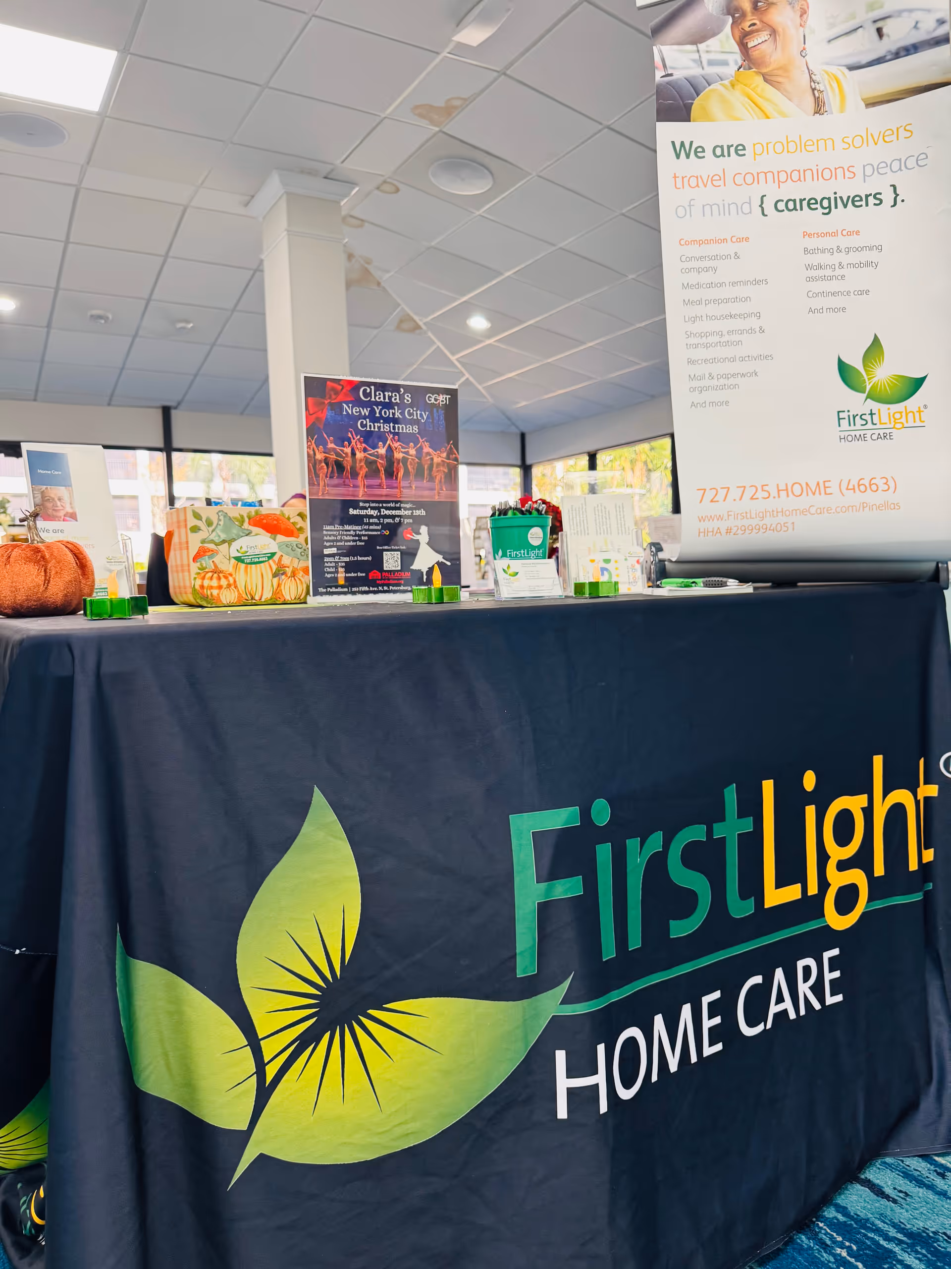 Indoor reception area with a FirstLight Home Care table, banners, and promotional materials on display.