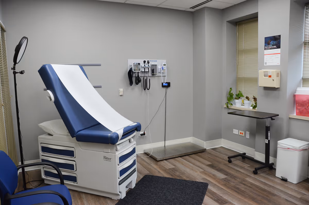 Blue and white medical examination chair in a clinical room with equipment and plants.