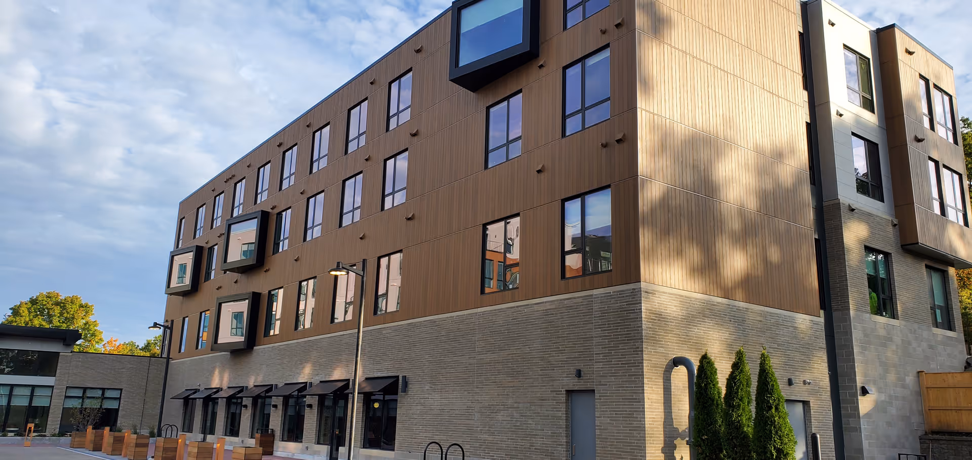 A modern four-story senior living building exterior with brown siding and large windows.