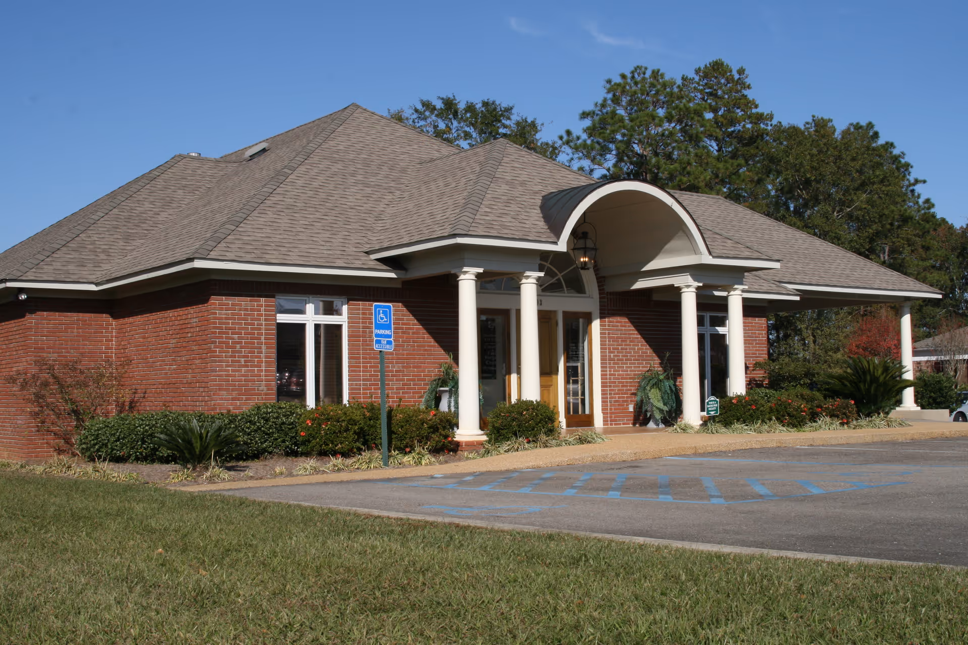 Brick clinic entrance with curved portico, white columns, and manicured landscaping.