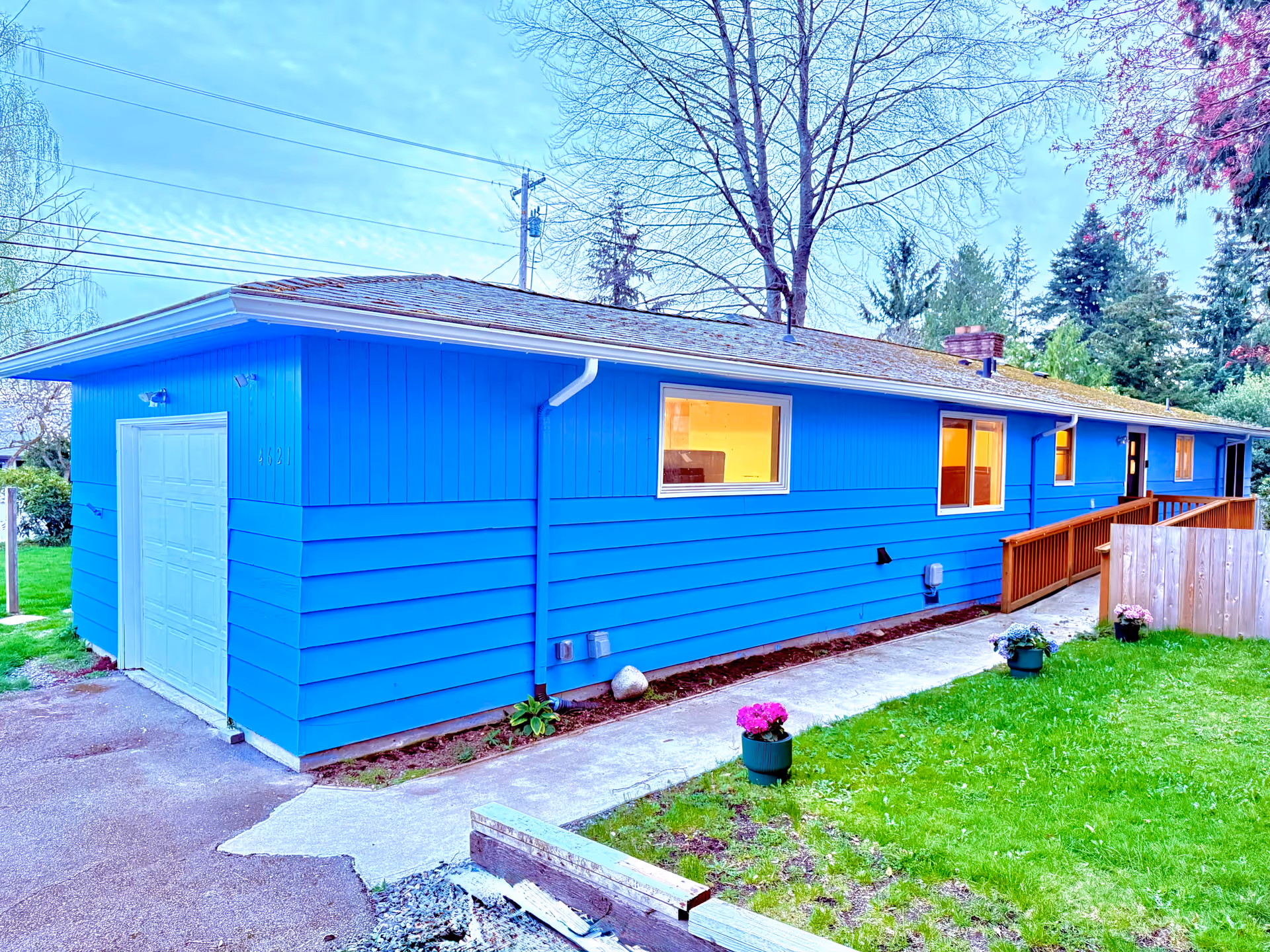 Bright blue single-story care home exterior with windows, a wooden ramp, and potted flowers along lawn.