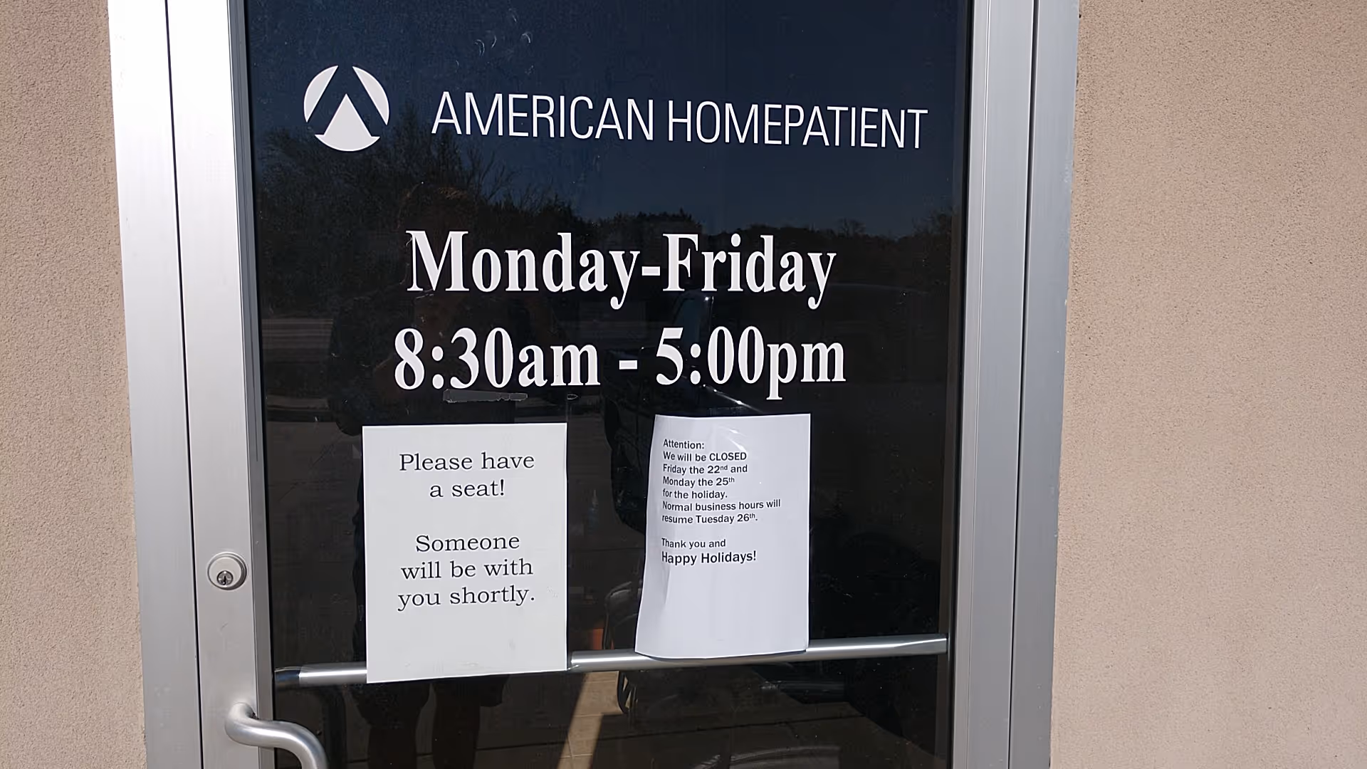 Glass door of American Home Patient displays hours and posted notices.