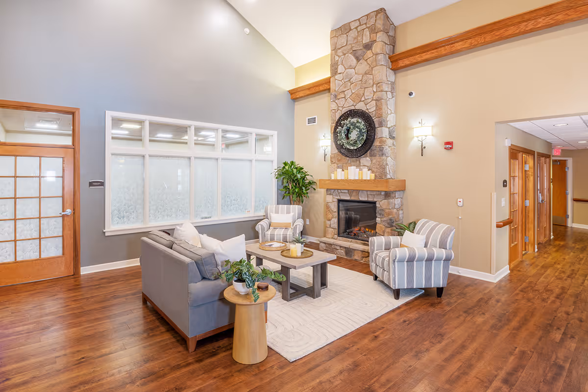 Bright communal living room with sofas and armchairs arranged around a stone fireplace and coffee table.