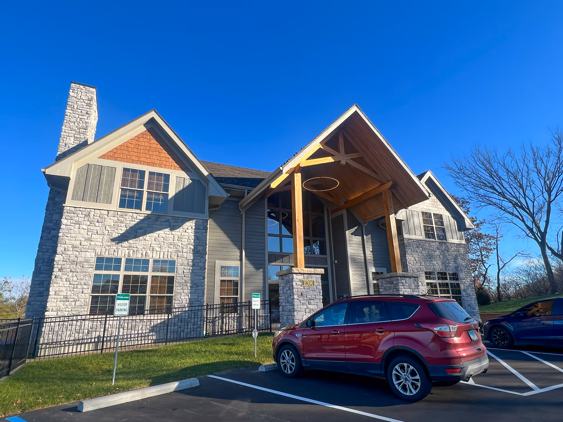 Front entrance of a stone-and-wood senior living facility with parked cars.