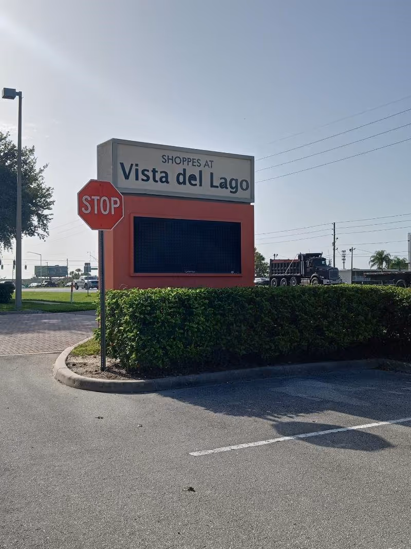 Outdoor parking lot with a red Vista del Lago sign and green hedge.