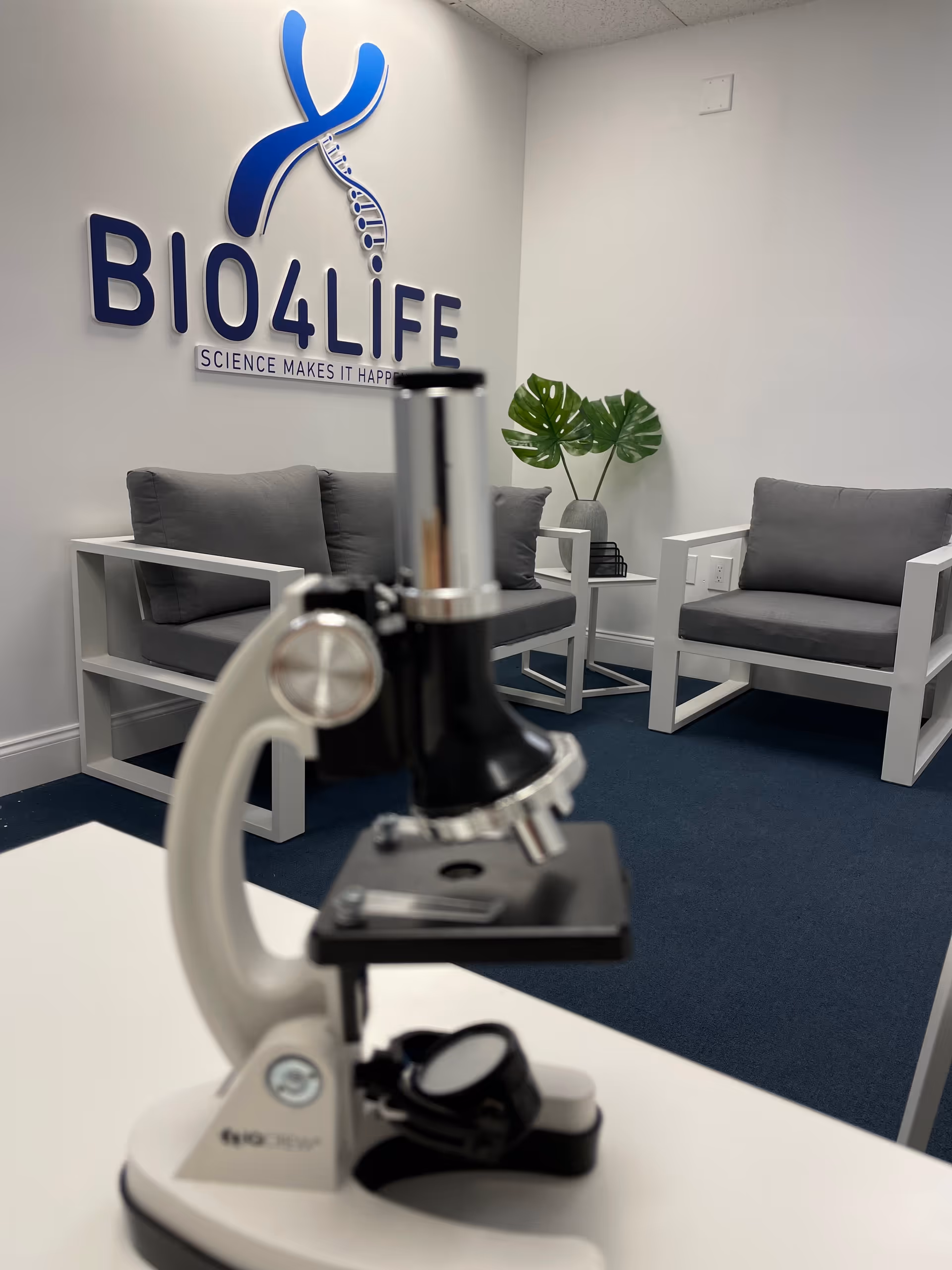 Microscope in foreground with a lounge area and a BIO4LIFE sign on the wall.